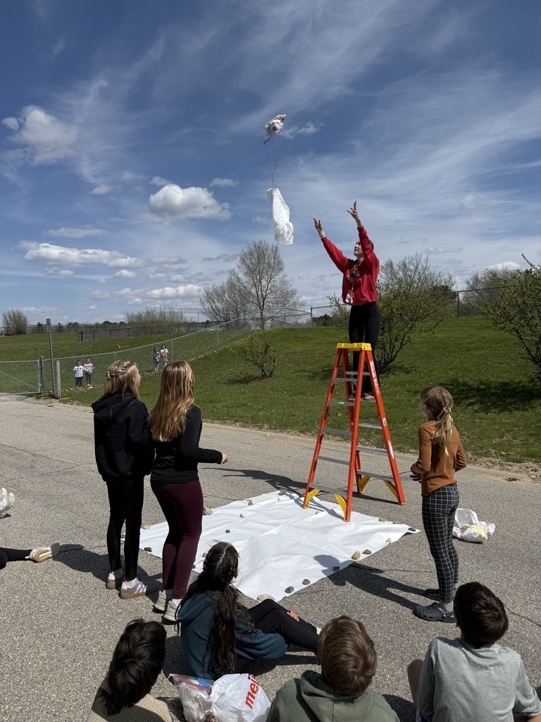People standing on a ladder throwing bags of eggs into the air, while others watch from below.