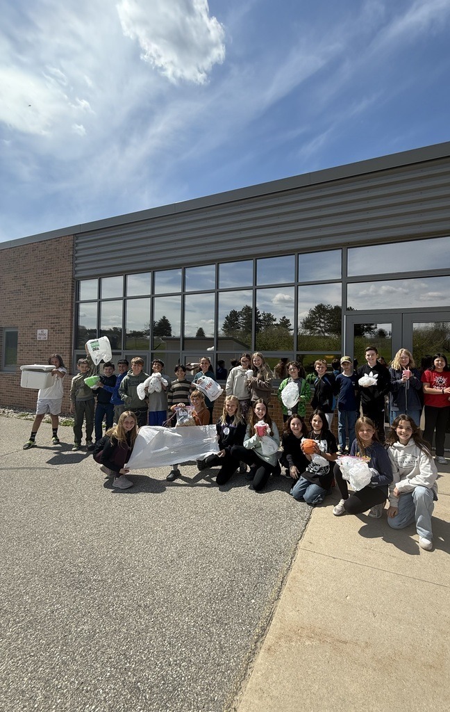 A group of people in front of a building, some kneeling, holding bags and banners.