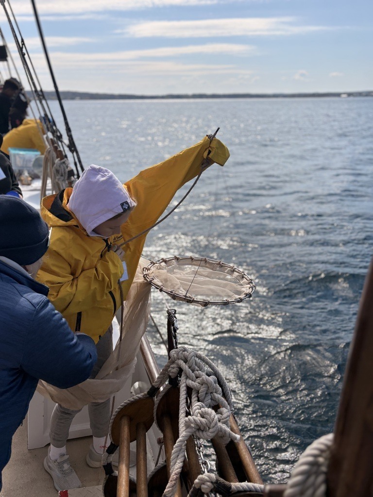 Two people in yellow and blue jackets on a boat, one holding a net, over calm ocean water.