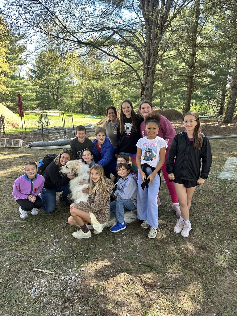 Group of children and young adults, two holding a large white dog, posing for a photo outside on a dirt field.
