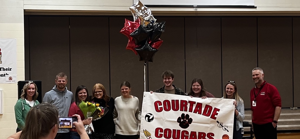 A group of people stand behind a banner that reads "COURTADE COUGARS" in a room.