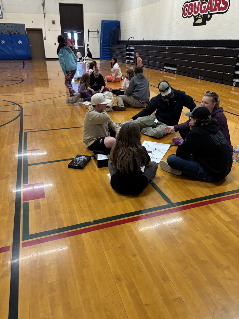 Group of people sit in a circle on a basketball court with a wall that says Cougars.