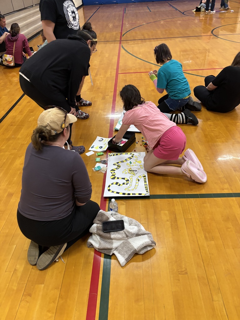 A group of adults and children are seated on the floor of an indoor court, engaged in a game.