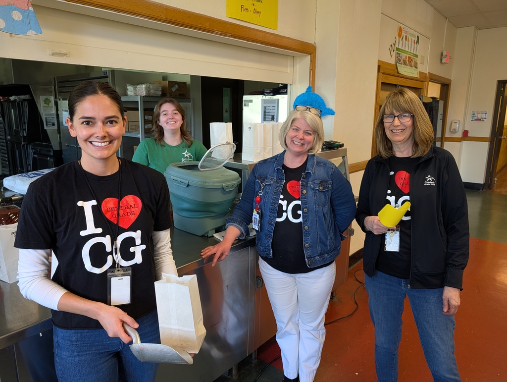 Four women stand in a room, each wearing black t-shirts and jeans. Two have white pants, and one wears a denim jacket.