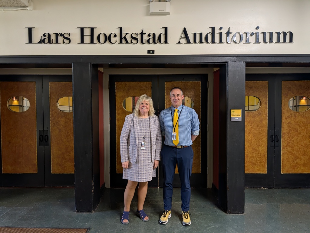 Two people stand in front of the Lars Hockstad Auditorium. The sign above them has large letters.