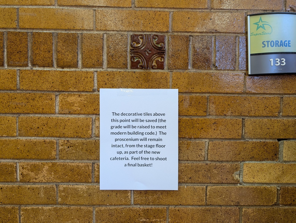 White sign attached to a brick wall reads "The decorative tiles above this point will be removed the grade will be raised to meet modern building code."