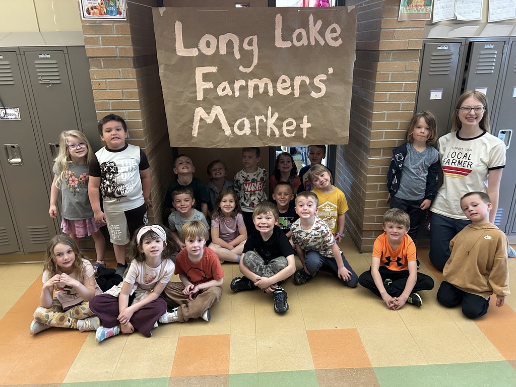 A group of children in front of a sign that reads "Long Lake Farmers' Market" inside a room.