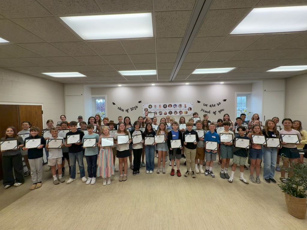 A group of students poses for a photo with certificates in a room with white walls and wooden floors.