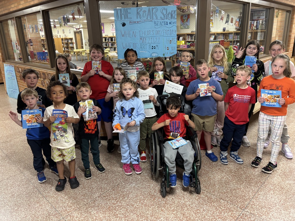 A group of children in a library pose for a photo. They hold books and wear casual clothing.