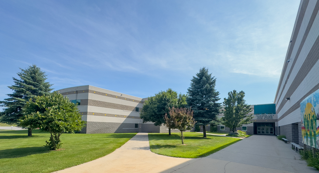 A school with a grassy lawn, trees, and a paved path leading to the entrance.