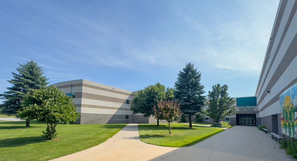 A school with a grassy lawn, trees, and a paved path leading to the entrance.
