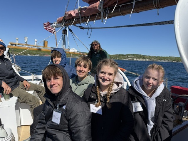 A group of people on a boat in a body of water. They are wearing jackets and some have braids.