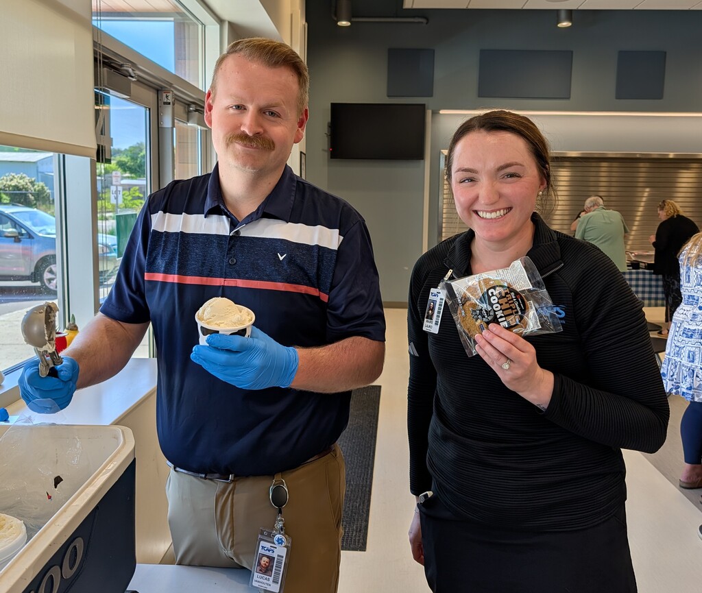 Two people stand in a kitchen area, one with a scoop of ice cream and the other holding a package.