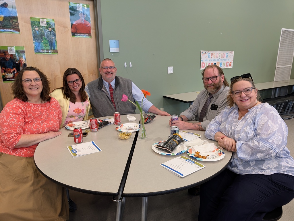 Five people sit around a table with food and drinks. Two women wear glasses. One woman has sunglasses on her head.
