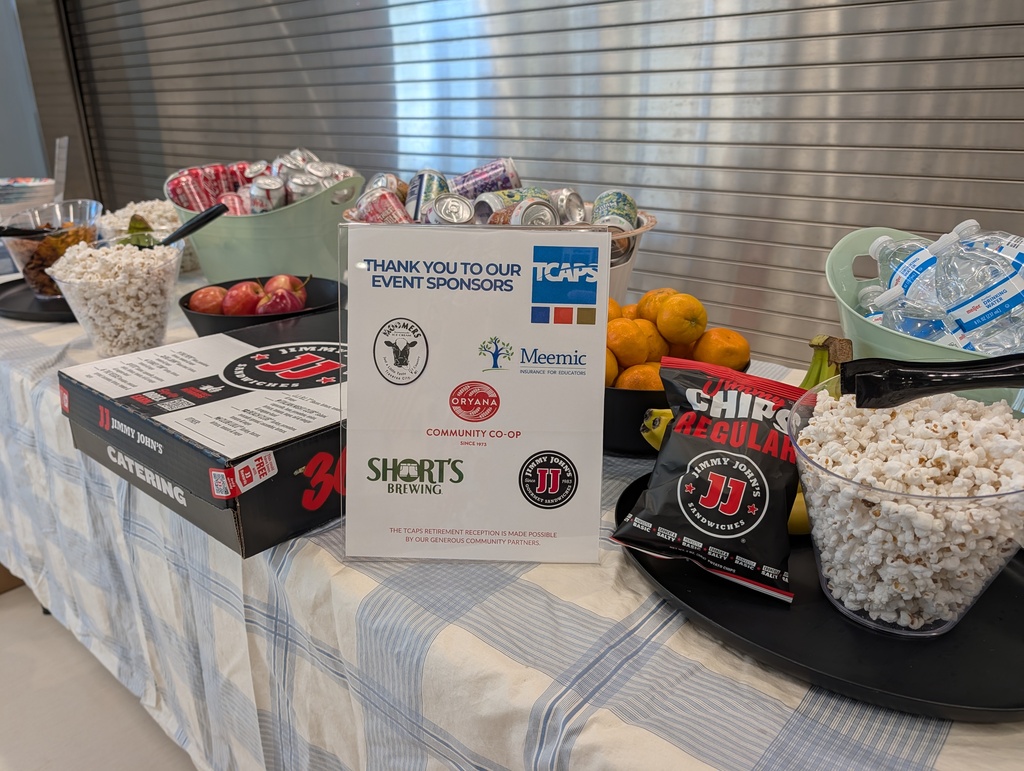 Table with a blue-white checked tablecloth holds bowls of popcorn, candy, fruit, and snacks. A black tray holds a sign for Shorts Event.