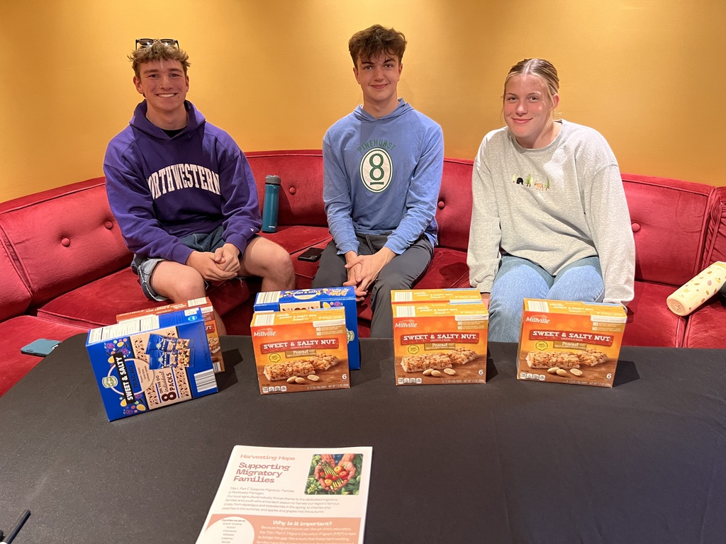 Three people sit on a red couch with boxes of food in front of them. One holds a blue bag.