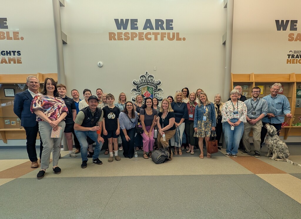 A group of people, some holding items, pose for a picture in a lobby. Behind them, a wall displays the words "We Are Respectful."