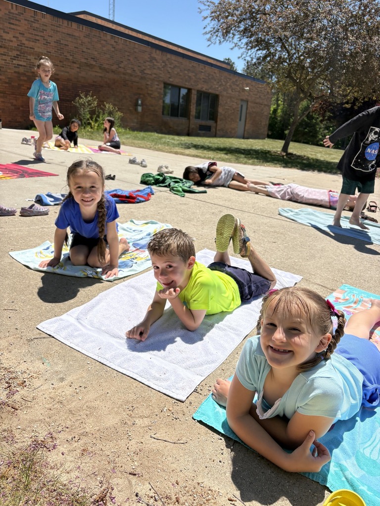 Several children are lying on blankets in an outdoor area in front of a brick building.