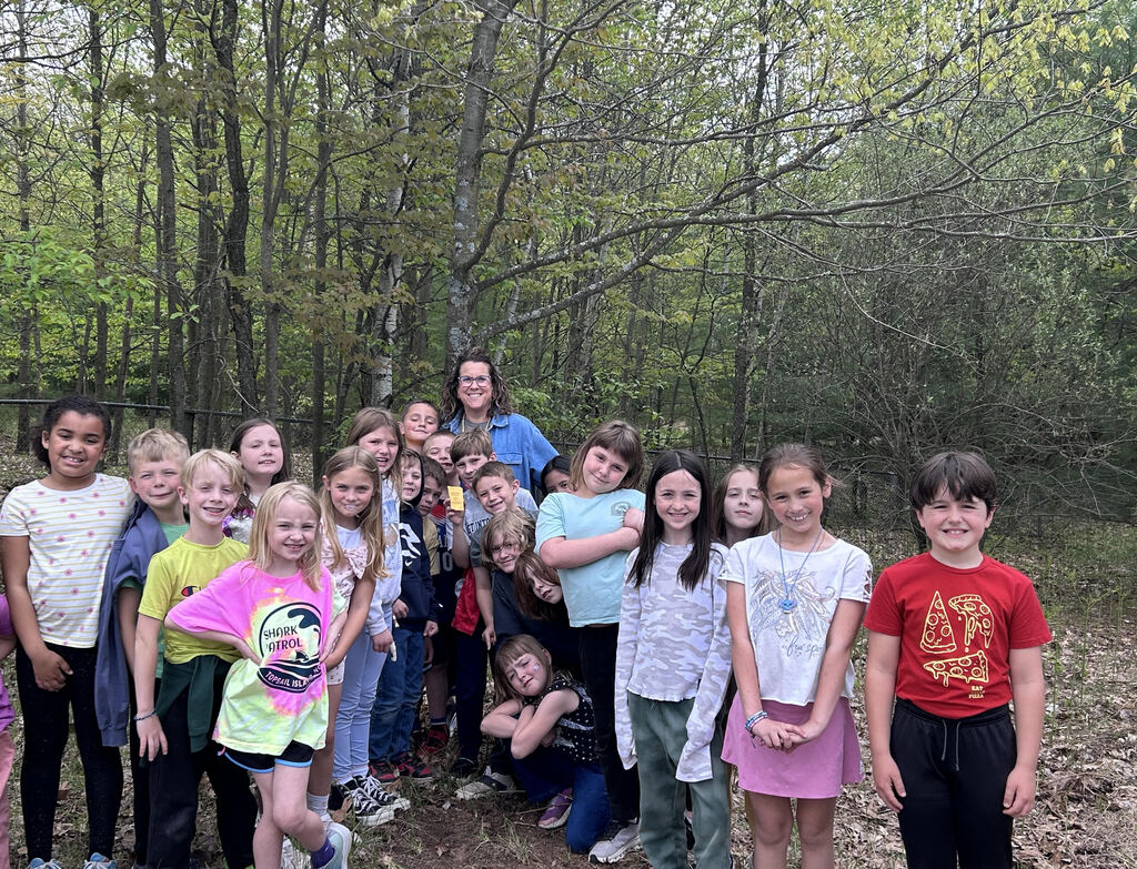 A group of children in various colored shirts and pants poses in a wooded area.