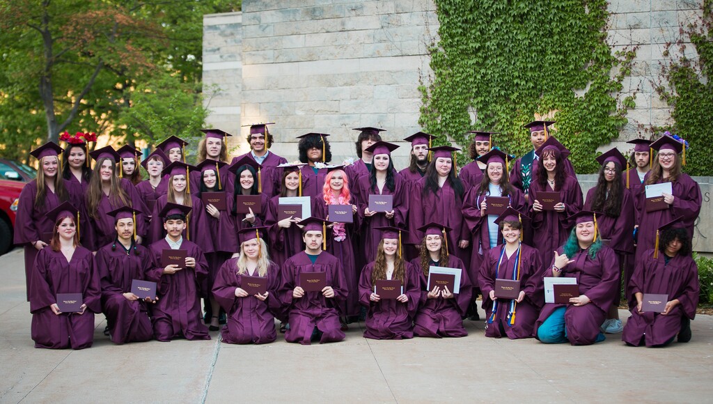 A group of people wearing purple graduation gowns and caps, posing for a photo in front of a building.