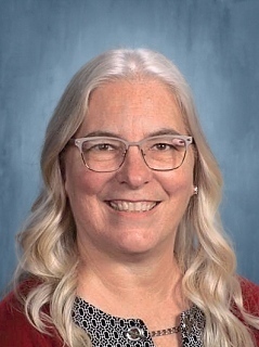 A woman with long blonde hair wearing glasses and a red top is smiling for the camera.
