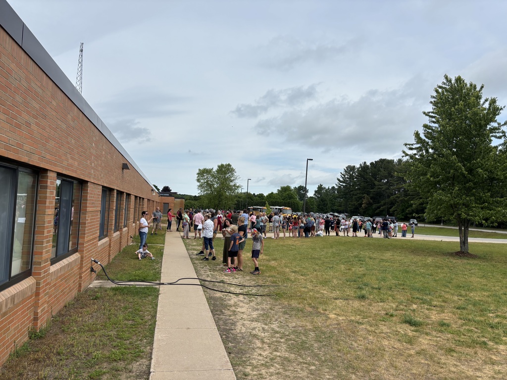 Group of people standing and walking on a sidewalk in front of a building with brick walls.