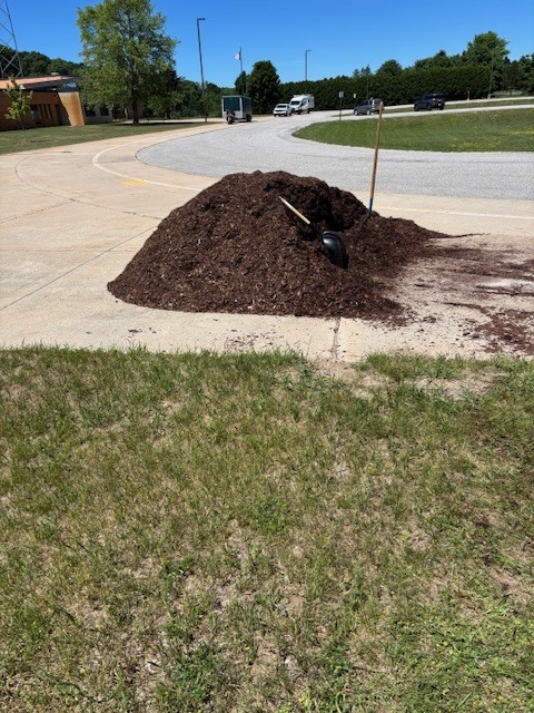 A pile of mulch is on the side of a paved road, with a shovel buried inside.