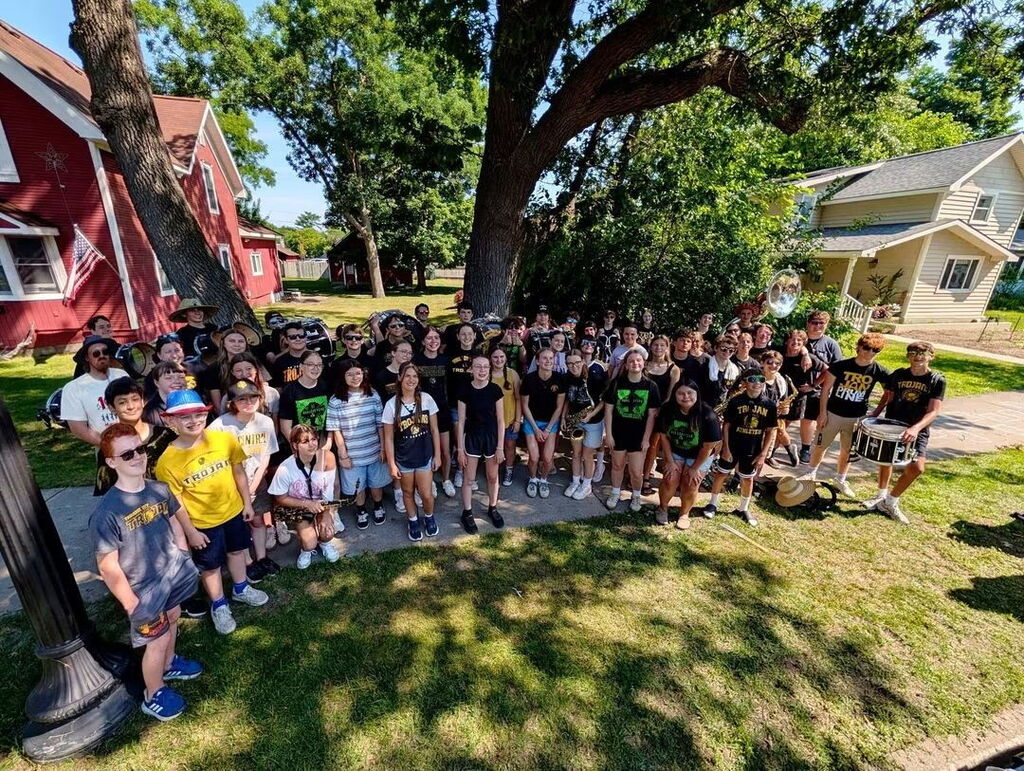 A large group of students pose for a photo outdoors with some holding musical instruments.