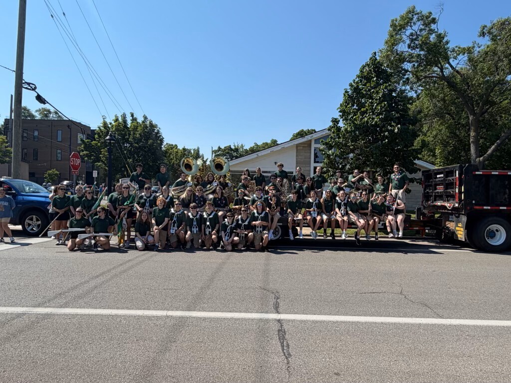 A marching band sits on a decorated float, playing instruments.