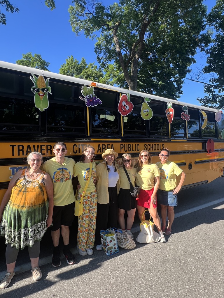 Six individuals, wearing yellow t-shirts, stand in front of a decorated yellow bus on a street.