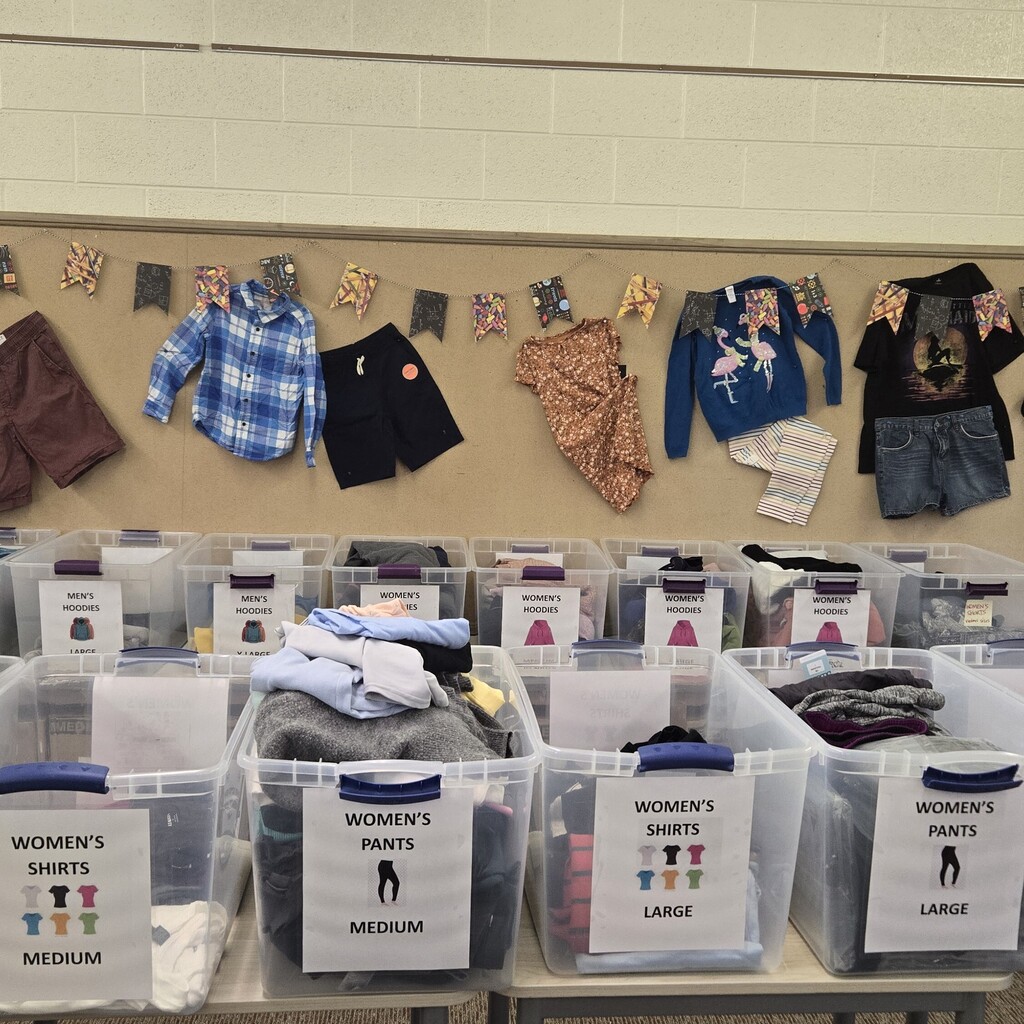 A room with organized clothing items. Plastic bins labeled "Women's Shirts" and "Women's Pants" on a table.