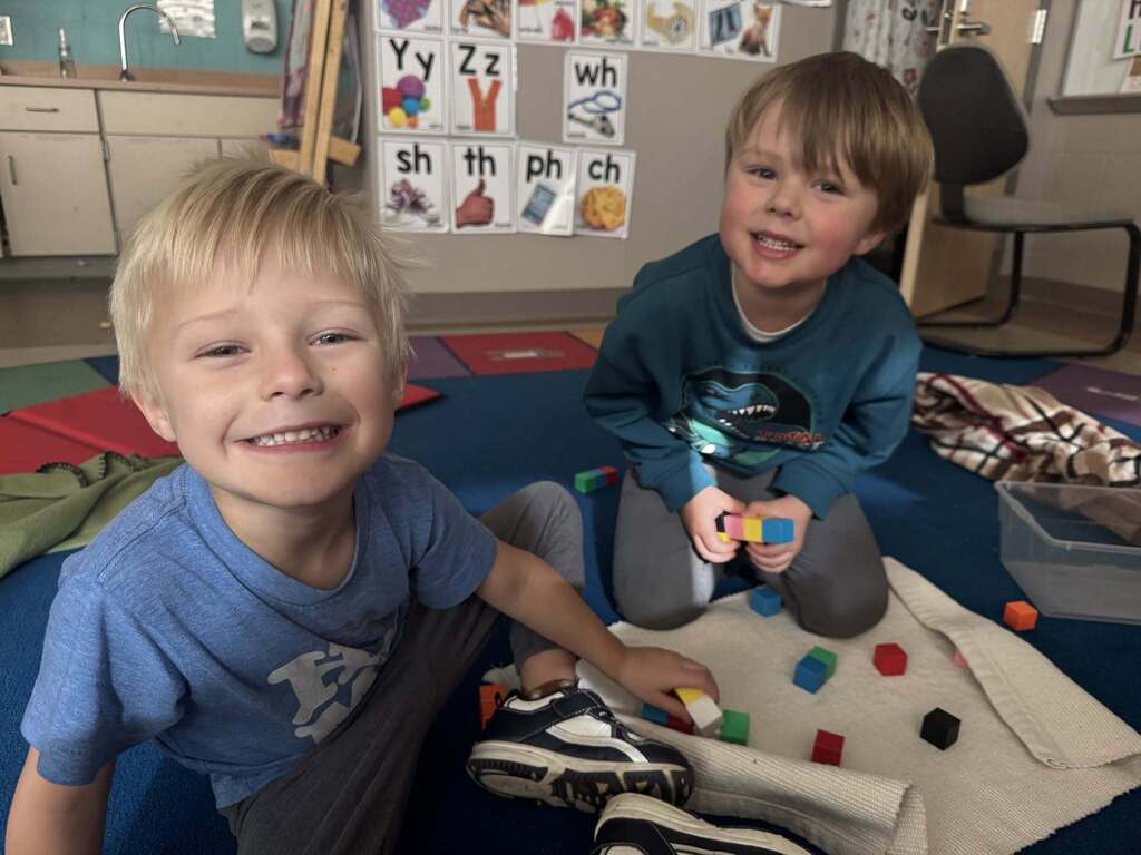 Two children, one in a blue shirt and the other in a dark blue shirt, playing with colorful cubes.