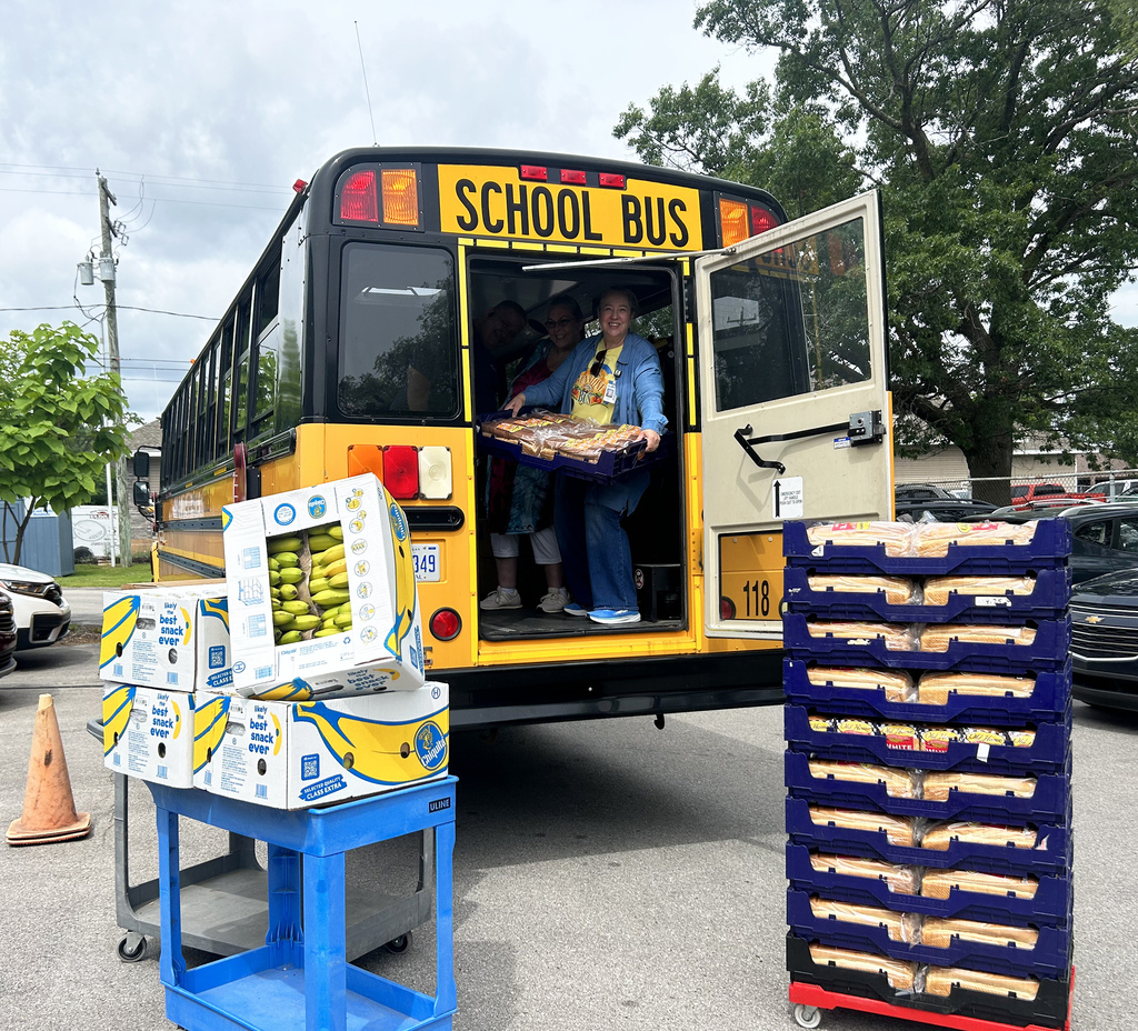 A school bus with an open door. A person inside holds a tray. Two people sit inside.