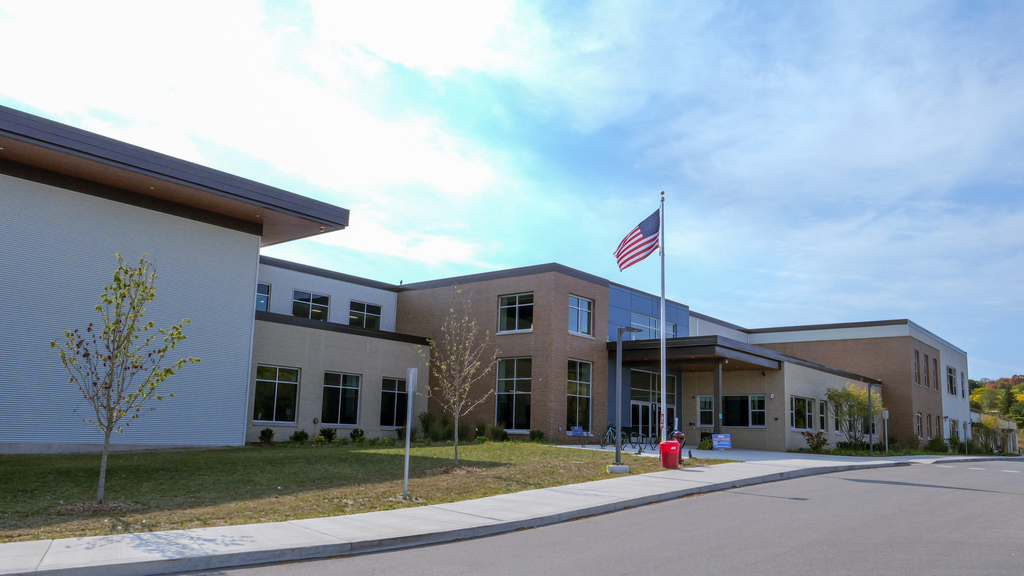 A building with an American flag. The entrance is on the right. Trees and grass surround the building.