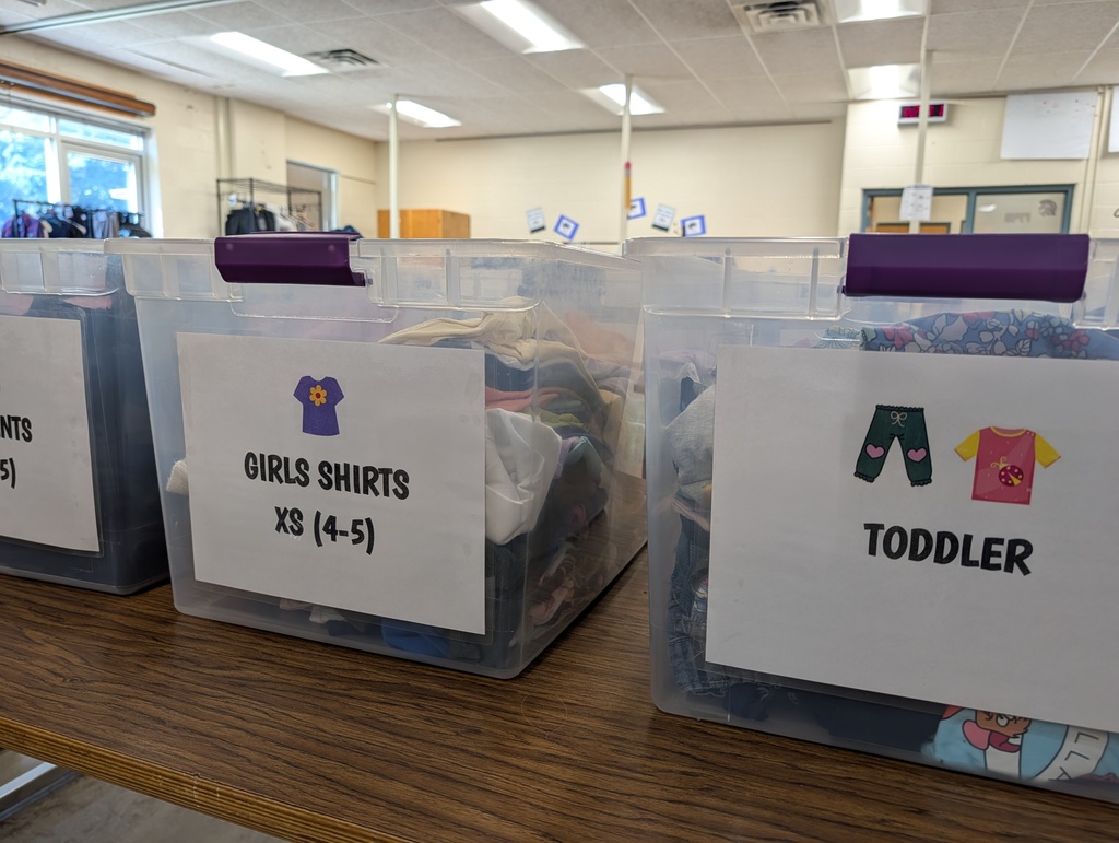 Four clear plastic bins on a wooden table. Labels on bins read "Girls Shirts XS (4-5)", "Toddler", and "Sizes".