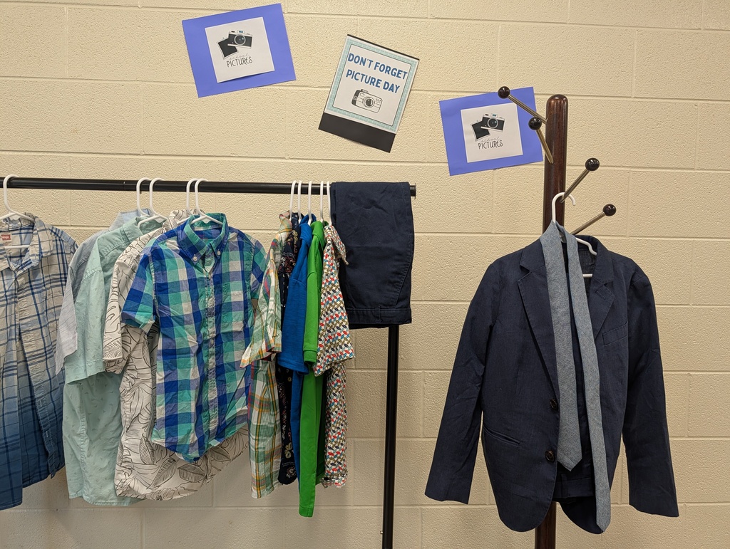 A clothing rack displays various shirts and a suit jacket on a white wall, with three blue signs attached above.