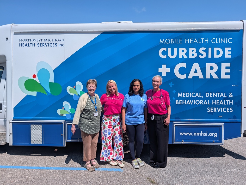 Four people stand in front of a blue and white mobile health clinic vehicle labeled "Curbside + Care."