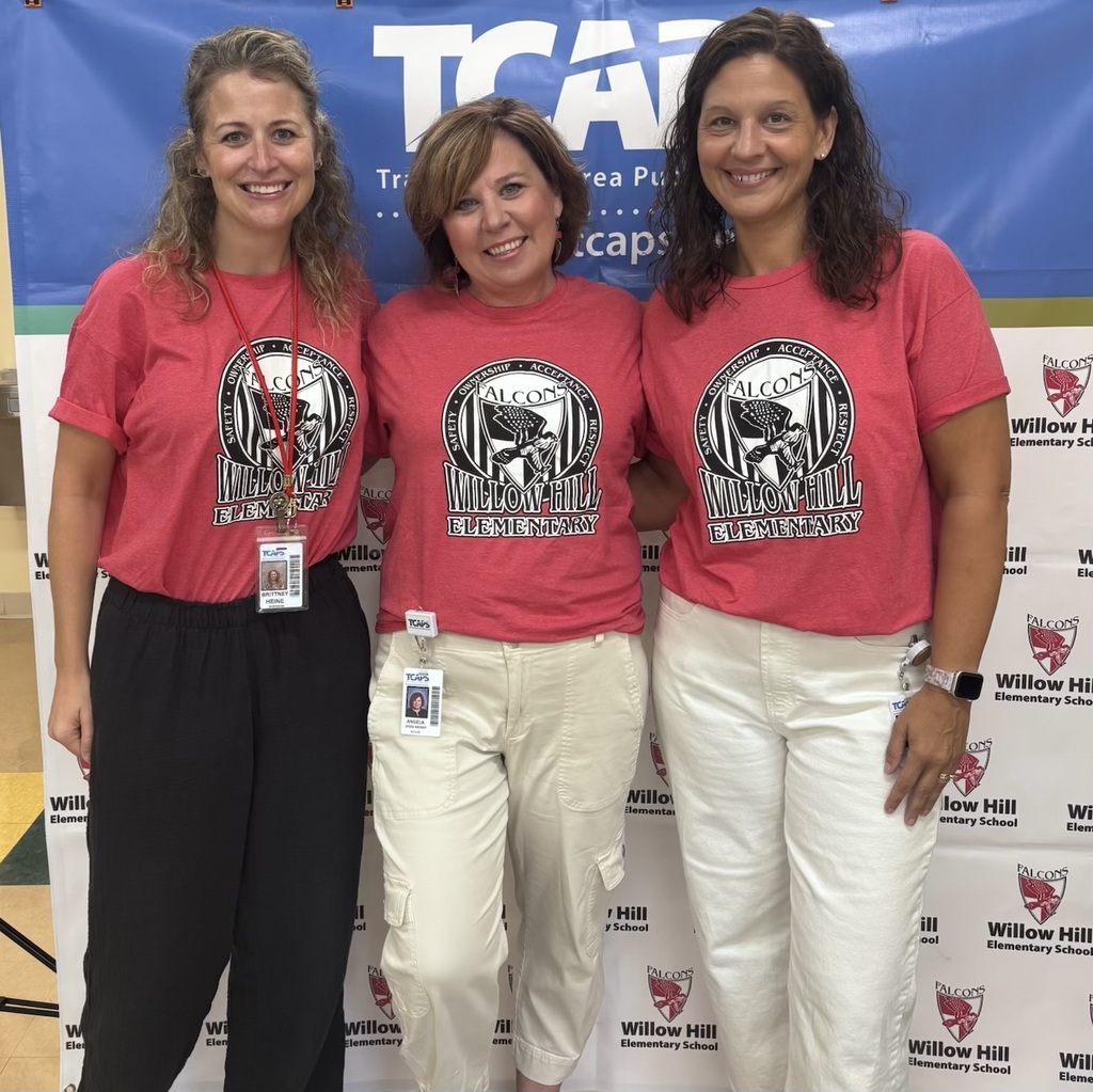 Three women wear matching red t-shirts and stand in front of a blue banner.