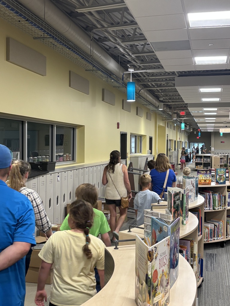 A group of people move through a brightly lit hallway in a library with yellow walls and bookshelves.