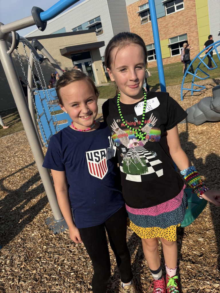 Two girls, one in a blue shirt and the other in a black shirt, standing next to playground equipment.