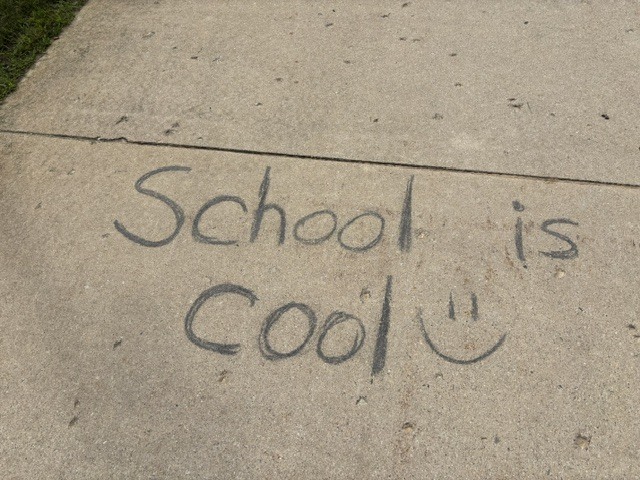 Sidewalk with the message "School is Cool" written in black chalk, accompanied by a smiley face.