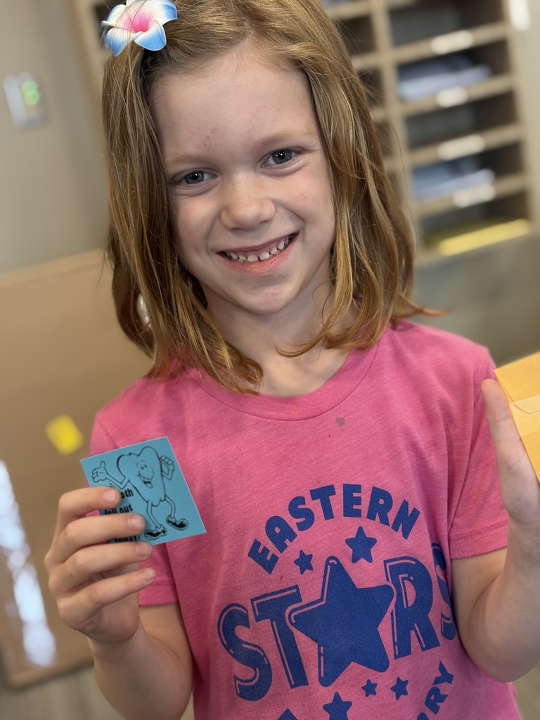 Girl in pink shirt holds a small drawing of an elephant, smiling and showing it to the camera.