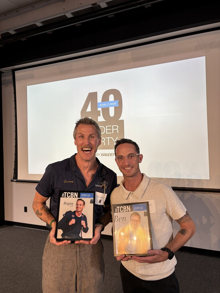 Two men hold up magazines in front of a screen. A projector screen displays the number 40.
