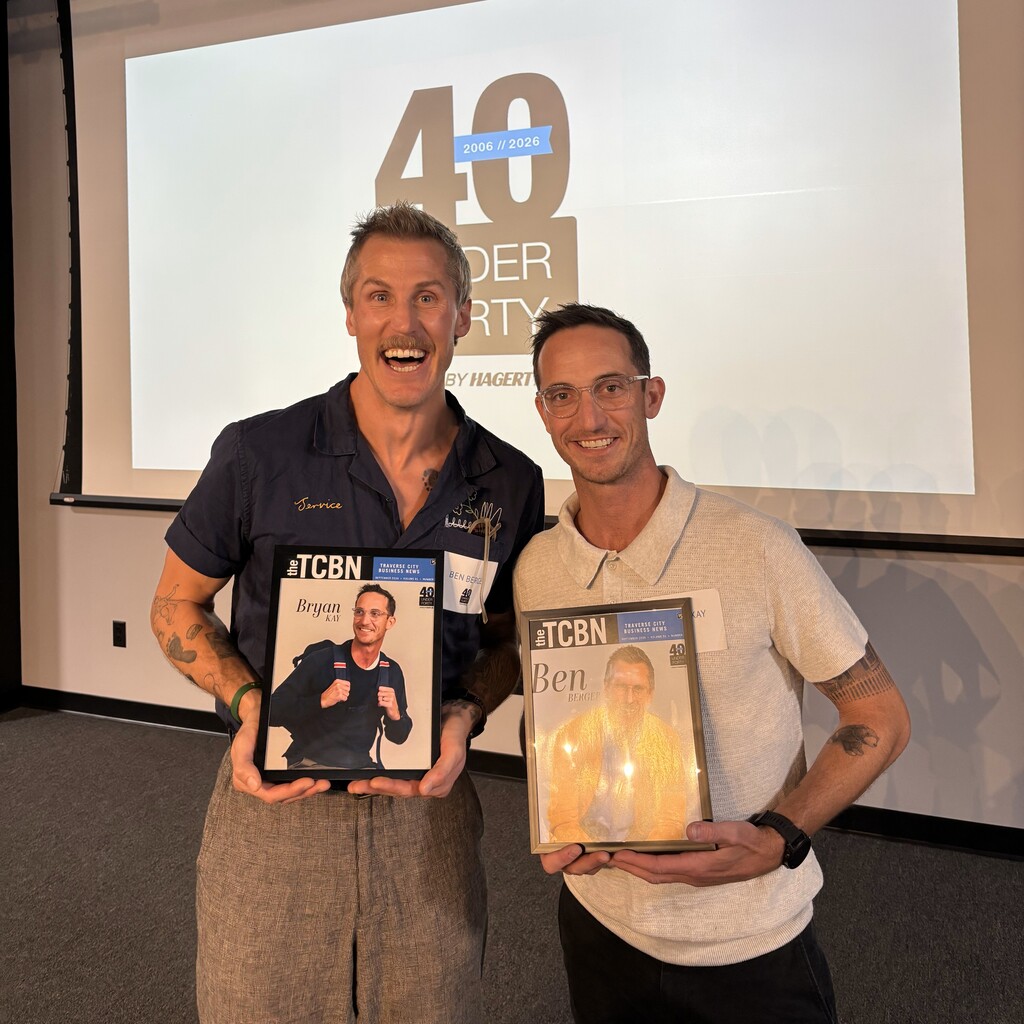 Two men holding magazines with photos of people in front of a projection screen.