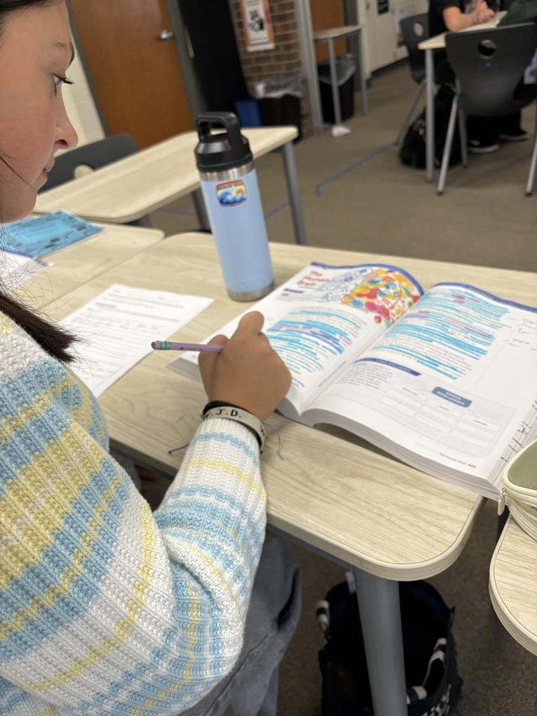 A person is seated at a desk, studying an open book. A water bottle and a pencil are on the desk.