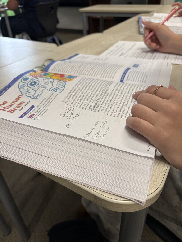 A person writes in a notebook. A book is open with a section on the human brain.