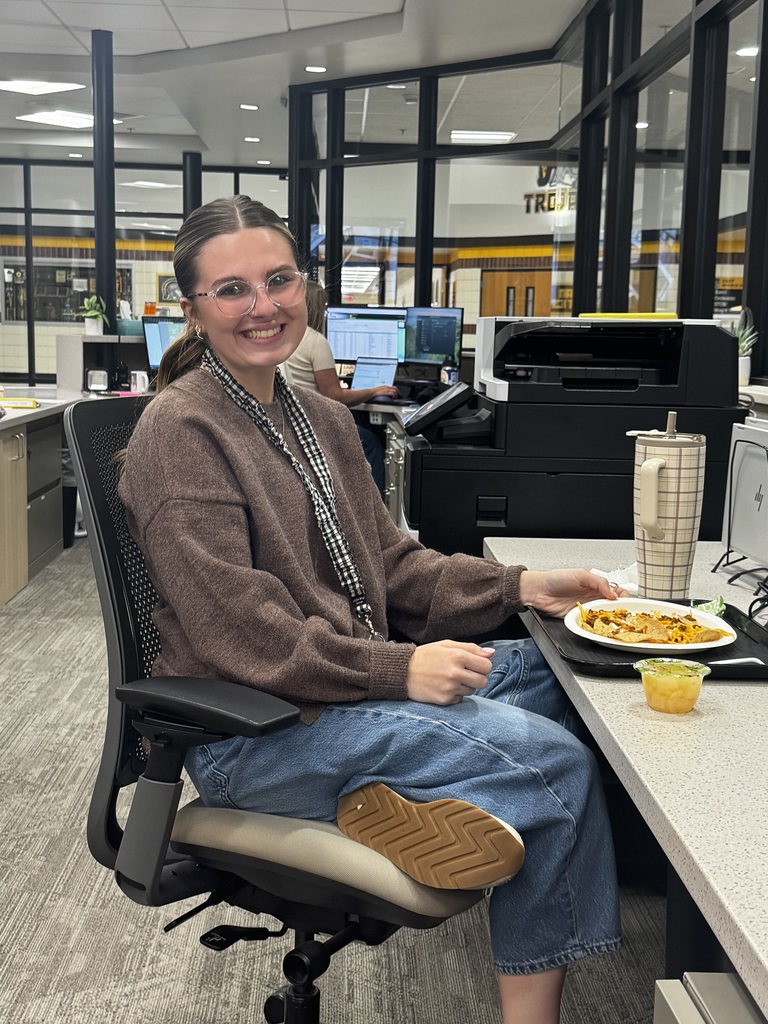 Person sitting at a desk with a plate of food. Behind them is a printer.