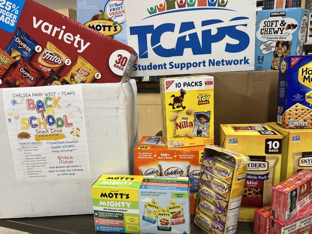 A display of various packaged food items, including snacks and boxes, on a table with a sign reading "TCAPS".