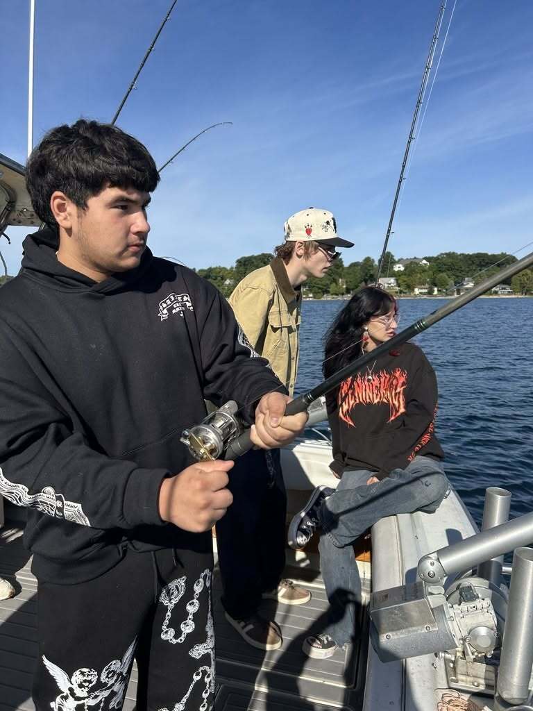 Three people on a boat, one holding a fishing rod, another with a hat, and one sitting.