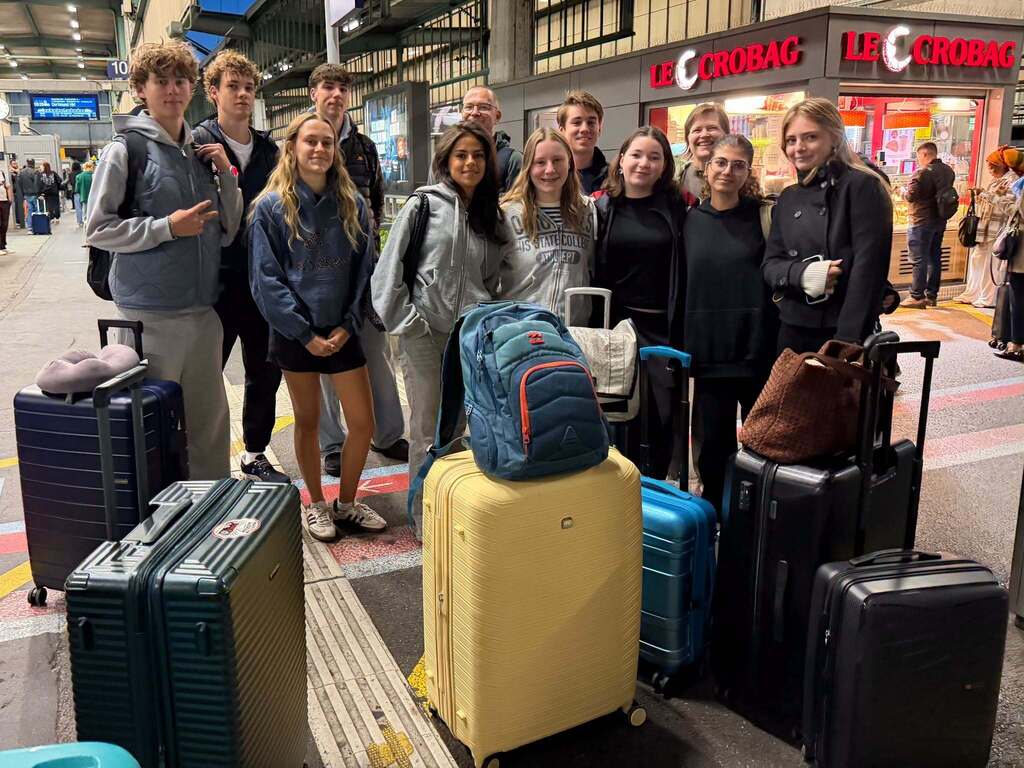 A group of people standing in a station with various suitcases and bags in front of them.